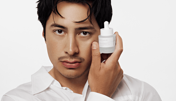 Hudson looks into the camera and holds a dropper bottle of ampoule beside his cheek.