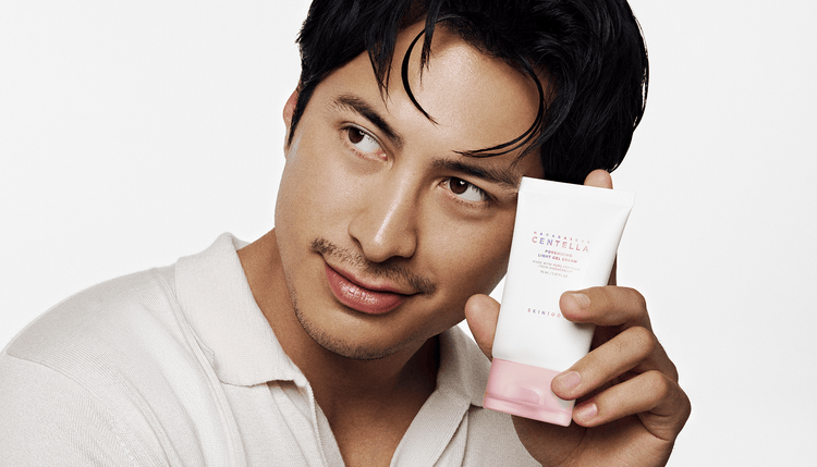Hudson glances sideways while holding a gel cream tube beside his face.