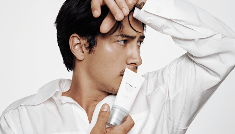 Hudson raises one arm over his head and presses a skincare tube against his chin.