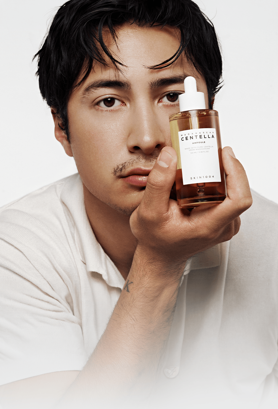 Hudson Williams holding a bottle of SKIN1004 Madagascar Centella Ampoule beside his face