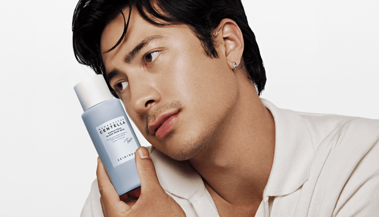 Hudson holds a bottle of Glass Skin Milk against his cheek and looks to the side.
